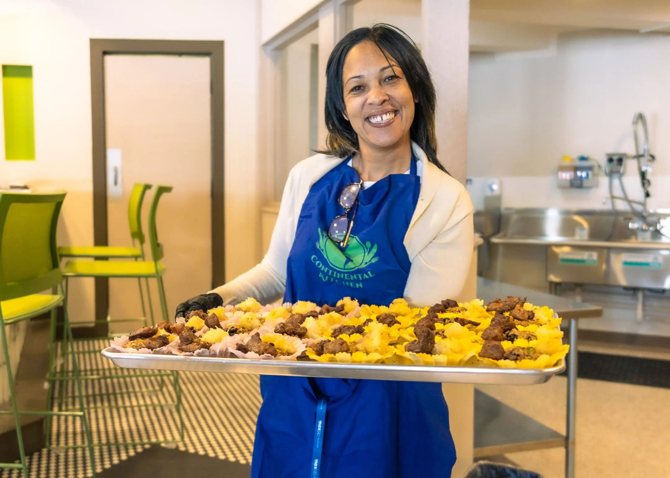 Continental Kitchen, photographed by AVO Dynamics: a smiling member in a Continental Kitchen apron holds a full tray of food in the shared kitchen