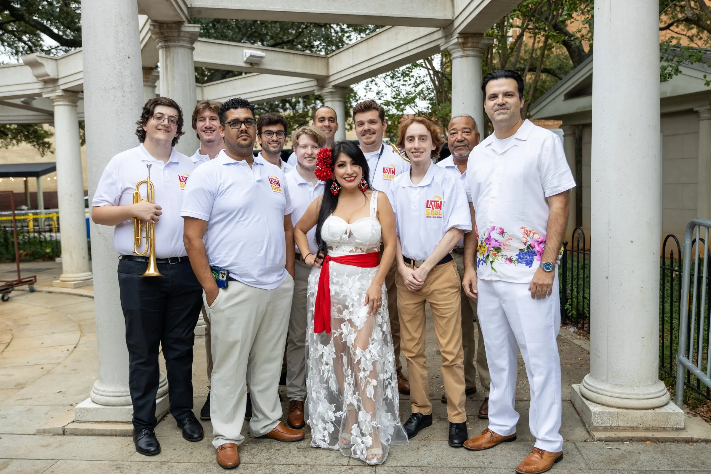 A band dressed in white poses with a performer in a white gown and red sash, photographed by AVO Dynamics at Mobile Latin Fest 2023