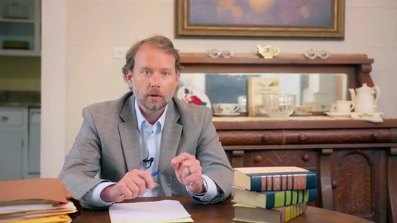 Alex Odom speaks to camera from behind a desk stacked with law books, from a campaign video AVO Dynamics made for Alex Odom's 2022 run for District Judge